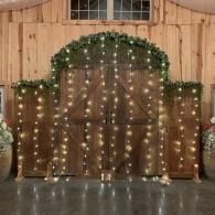 Barn doors framed with greenery and white string lights in a rustic wooden venue