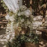 White floral arrangement on a wooden post with draped fabric in an outdoor setting