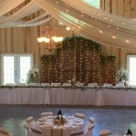 Elegant wedding reception hall with draped ceiling, chandeliers, and a decorated head table backdrop