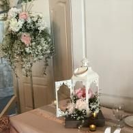 White lantern centerpiece with pink and white flowers on a decorated table beside a floral arrangement.