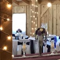 Rustic barn reception with string lights, white-draped tables, and floral centerpieces.