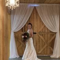 Bride in white gown holding bouquet in front of wooden barn doors with draped white curtains