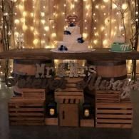 Rustic wedding dessert display with a cake, candles, and warm string lights on a wooden table