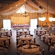 Elegant banquet hall with draped white fabric, chandeliers, and round tables set for a formal event