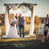 Wedding couple under floral arch in an outdoor field ceremony