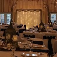 Elegant banquet hall with round tables, white chairs, and warm amber lighting around a curtained stage