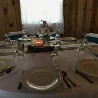 Set dining table with white plates, glasses, candles, and a floral centerpiece by a window