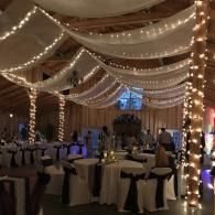 Decorated banquet hall with draped fabric, string lights, and round tables set for an event