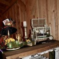 Vintage shelf with a green teapot, lamp, flowers, and a decorative miniature greenhouse against wood paneling