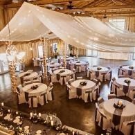 Elegant rustic banquet hall with round tables, white drapery, and warm string lights overhead