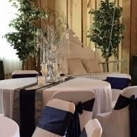 Round tables with white cloths and navy chair sashes in a decorated indoor event space