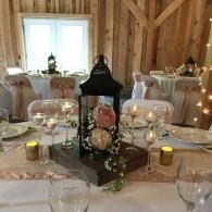Elegant banquet table with candles, flowers, and lantern centerpiece in a rustic, wood-paneled room