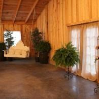 Wood-paneled hallway with potted plants, sheer curtains, and a white bench near a bright doorway