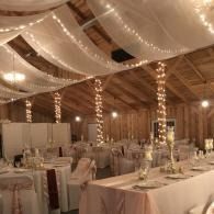 Elegant indoor banquet hall with white draped ceiling, string lights, and set tables and chairs