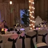 Decorated banquet hall with white-covered chairs, round tables, and string lights around a pillar