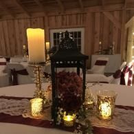 Candlelit rustic table centerpiece with lantern, pillar candle, and floral decor in a wood-paneled room