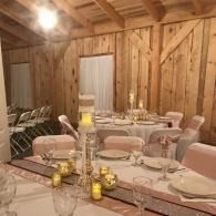 Rustic barn dining room with a long set table, candles, and pale pink chairs