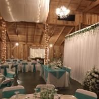 Rustic barn-style reception hall with teal table runners, white drapery, and warm string lights