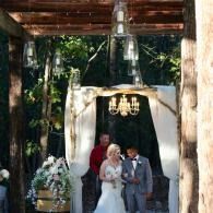 Bride and groom stand under a floral arch at an outdoor wedding ceremony