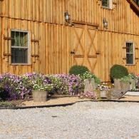 Rustic wooden barn wall with windows, flower planters, and a gravel foreground