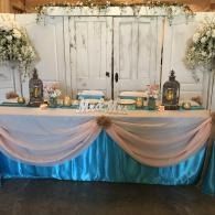 Decorated dessert table with pastel draping, white backdrop, lanterns, and floral arrangements