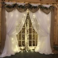 White draped curtains with warm string lights framing double doors at an event entrance