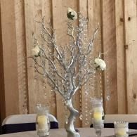 Silver decorative tree centerpiece on a table with candles against a wooden wall