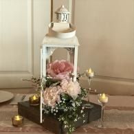 White lantern centerpiece with pink and white flowers and candles on a table