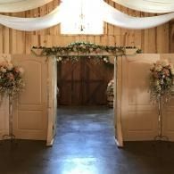 Open wooden doors beneath floral archways in a softly lit rustic venue entrance