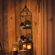 Decorative birdcage lantern with flowers and a glowing candle against a warm wooden wall