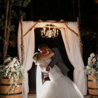 Bride and groom embracing under a white draped arch with chandeliers at night