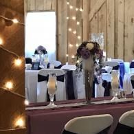 Decorated banquet table with white chairs, blue napkins, and floral centerpieces in a rustic wooden venue