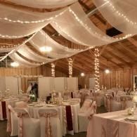 Decorated banquet hall with round tables, white draped ceiling, and warm string lights