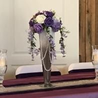 Purple and white floral arrangement with pearl strands on a silver vase at a decorated table