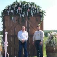 Two people standing before a large wooden floral backdrop outdoors