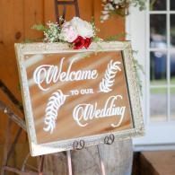 Wedding welcome sign on a white easel with pink flowers and greenery at the entrance to a venue