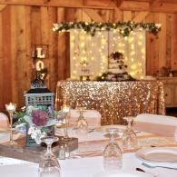 Rustic wedding reception table with string lights, gold décor, and a sparkling dessert display