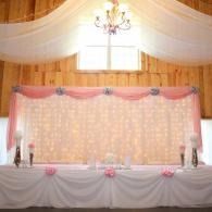 Decorated wedding stage with pink drapes, white backdrop, and chandelier in a banquet hall