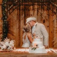 Couple kissing behind a wedding cake at a rustic ceremony backdrop