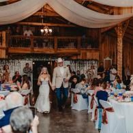 Bride and groom walking down a decorated wedding reception aisle among seated guests