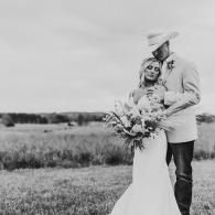 Bride and groom embracing in a field, holding a bouquet