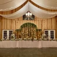 Decorated wedding reception table before a wooden backdrop with white drapes and string lights