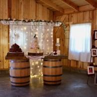 Rustic event display with two wooden barrels, string lights, and a draped table in a wood-paneled room