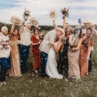 Wedding party cheering outdoors with hats raised in a field confetti shower