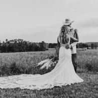 Couple embracing in a field, with the bride in a long white dress and veil