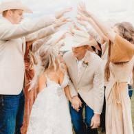 Wedding party dancing under a white canopy, with hands raised and smiling faces.