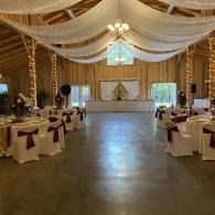 Elegant wedding reception hall with draped white ceiling, chandeliers, and decorated tables along a central aisle