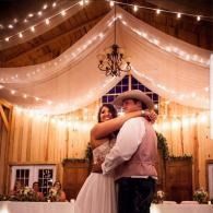 Couple embracing during a wedding dance in a warmly lit chapel with draped fabric and string lights.
