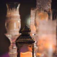 Ornate lantern glowing warm orange amid soft-focus glass candle holders and smoky light