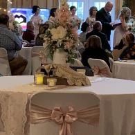 Decorated banquet table with floral centerpiece, candles, and a satin bow at an indoor reception